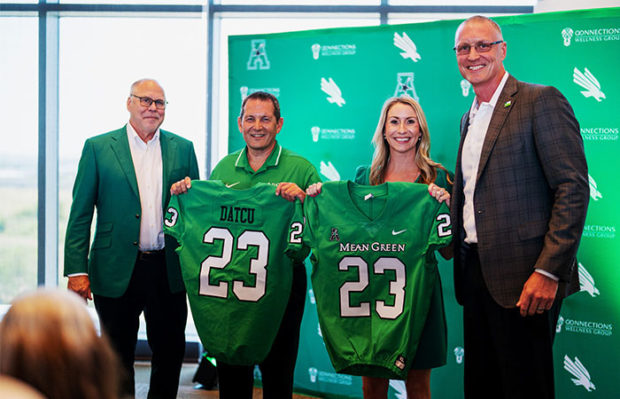 Image of four executives from DATCU showing off sport sponsorship shirts from UNT